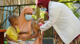 Una mujer con un niño en el regazo es vacunada por una profesional sanitaria.