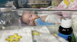 Un bebé yace en una cuna de plástico con un tubo de oxígeno en la boca.