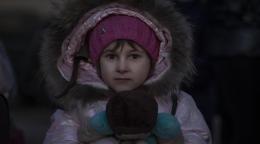 A young girl in a pink puffy coat holds a teddy bear.