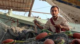 Un pêcheur yéménite de 27 ans est assis devant une embarcation et regarde l'objectif en tenant un filet de pêche dans les mains.