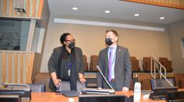 Une femme et un homme portant chacun un masque de protection respiratoire se tiennent debout derrière une table de conférence et discutent. 