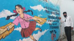 一个男人站在墙上的一幅画旁边，画中有一个女孩在挥舞翅膀。
