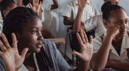 Teens raise their hands in an excited manner in a classroom setting.