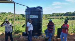 En Jamaïque, une femme et trois hommes se tiennent devant un réservoir d'eau installé dans un champ pour atténuer l'impact des sécheresses sur les hauts plateaux du pays.