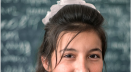 A close up of a girl smiling at the camera in front of a blurred out chalkboard.