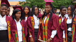Several young girls in predominantly purple graduation outfits stand before the camera smiling proudly. 