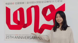 A young Chinese woman standing in front of a poster of a red ribbon