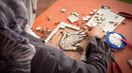 Une femme voilée est photographiée de dos en train de travailler avec des morceaux de mosaïque dans le cadre d'une atelier organisée par ONU Femmes.