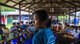 Au Myanmar, une jeune femme portant un polo bleu de l'UNICEF anime une session de partage entre pairs, entourée d'adolescents, dans un espace aménagé en extérieur.