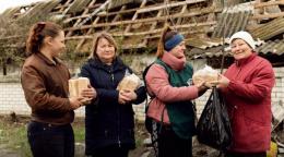 волонтер раздает женщинам буханки хлеба.