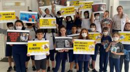 A group of students of elementary school age with their teacher. They are all wearing facemasks and standing side and proudly displaying their school work on waste management.