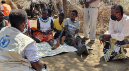 A group of people sit in a circle on the tan ground and discuss nutrition in Uganda