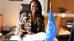 Woman in a colourful shirt sitting at a desk with a UN flag in the foreground