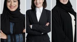 Three women in black clothes, two of them in headscarves smiling at the camera, side by side