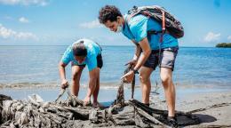 Two volunteers in blue t-shirts clean up parts of a beach