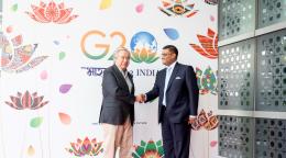 Two men in suits shake hands in India in front of a colourful banner
