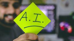 A man with a beard holds up a yellow stickie note, with "A.I" written on it.