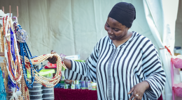 A woman in a black headscarf and striped dress runs her fingers through some jewellery