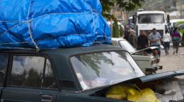 A car with bags loaded in the trunk and a bulky blue tarp on top.