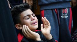 A young boy, with his hands to his face, cries in Gaza City.