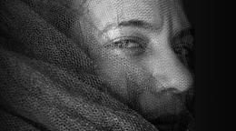 Черно-белая фотография женщины, лицо которой скрыто за тканевой сеткой.
