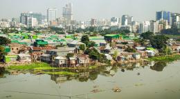 Трущобы поселения Дакки на фоне высоток Бангладеша рядом с загрязненной рекой