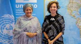 Two women - high-ranking UN officials - pose for a picture in front of a map and a UN flag.