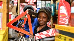 A woman in a headcap holds up a red sign inside a mechanic shed surrounded by tools