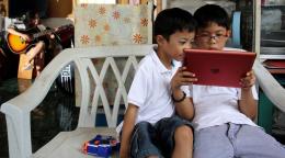 Два мальчика сидят на кресле и смотрят в планшет