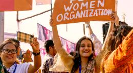 A group of women clad in orange taking part in a march, one of them holds up a sign saying "fund women's organizations"