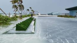 A scene of a beach in Maldives with water pooling by the shore where a green display stands.