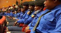 A row of women in blue police style uniforms with black berets, sitting on chairs