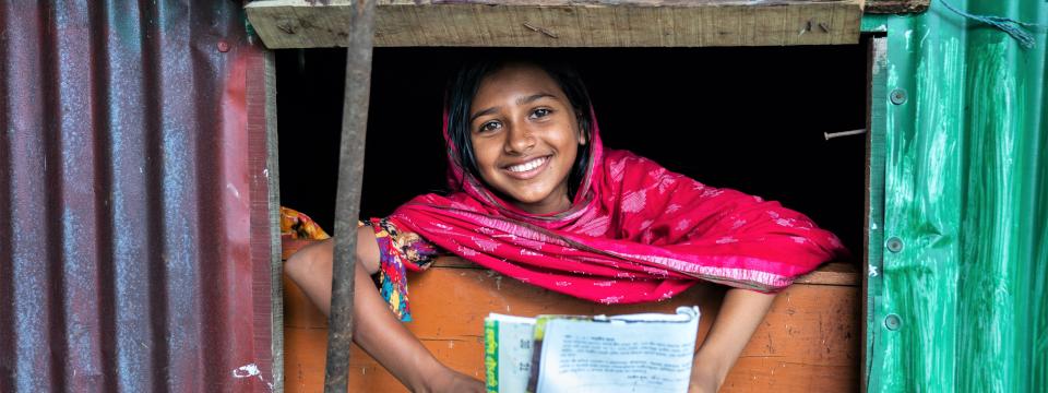 Woman holding a school book smiles brightly and leans out a window.