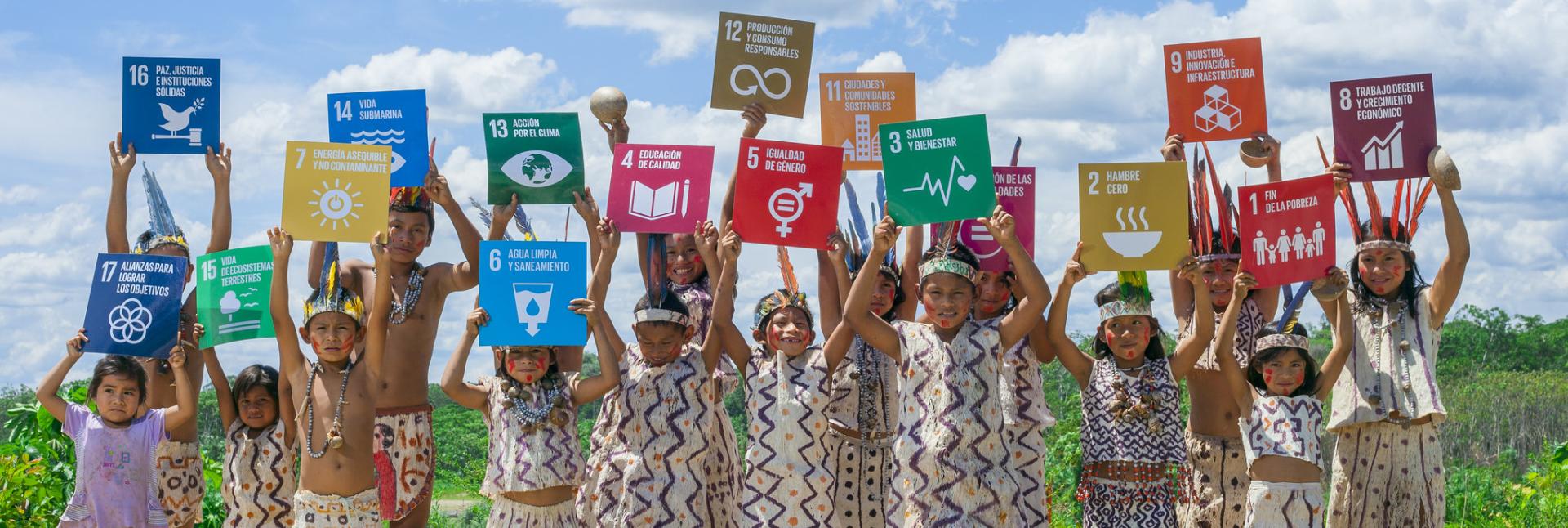 Children hold colorful signs of the SDGs on a sunny day. 