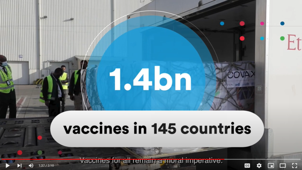 A screenshot stating "1.4 bn vaccines in 145 countries" in a blue-colored circle embossed on a picture of an airport hangar. 