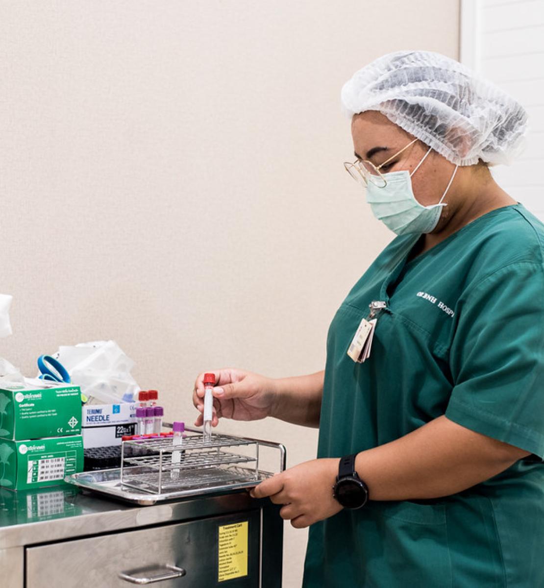 ممرضة ترتدي معدات الوقاية الشخصية وهي تجهز مواد الفحص الطبي.