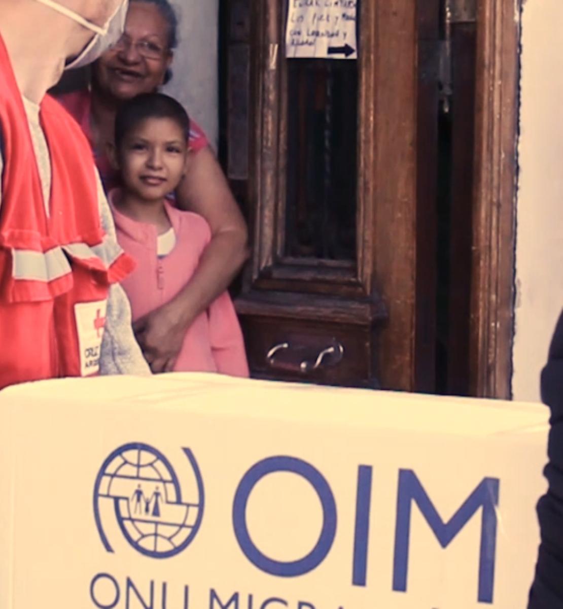 IOM staff carry a box of donations into a family's home.