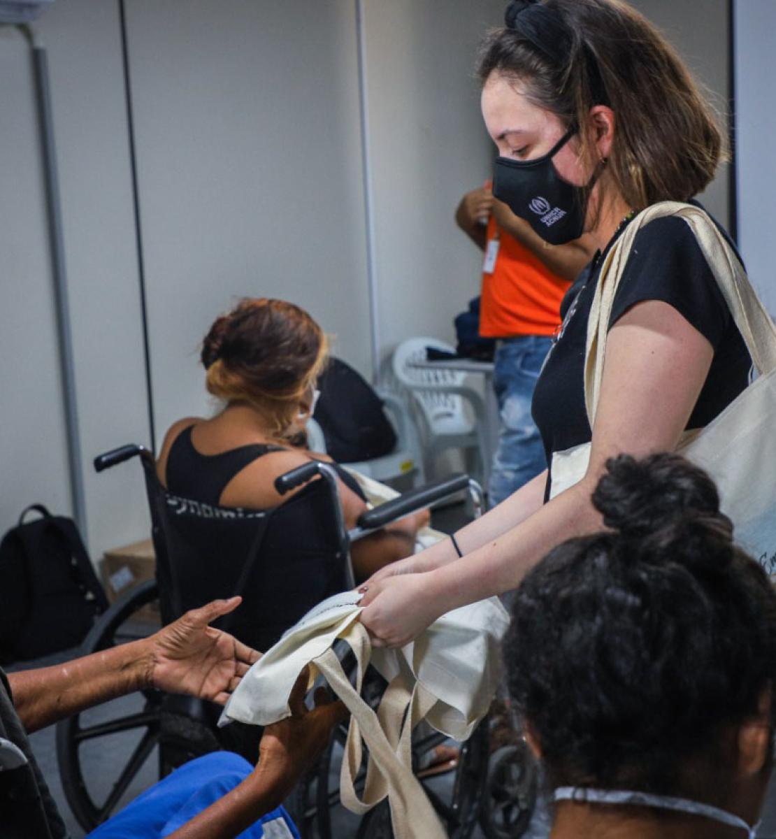 Plusieurs femmes, dont certaines en fauteuil roulant, sont réunies dans une salle pour recevoir une formation. Une femme membre du HCR portant un masque de protection tend à l’une des participantes un sac fourre-tout en tissu.