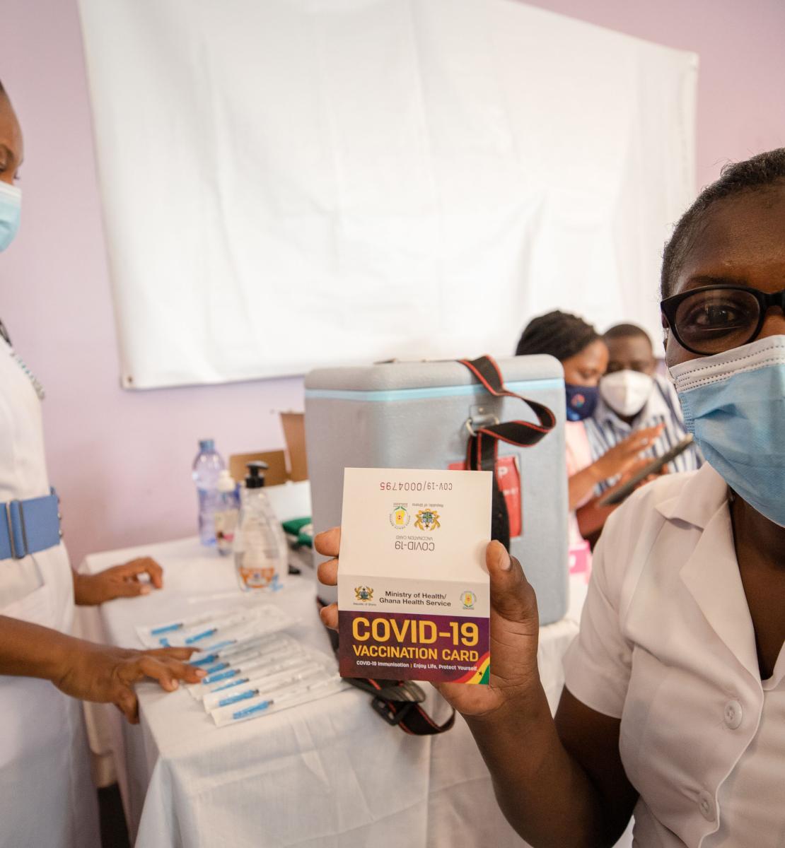 Una profesional de la salud en un centro de vacunación muestra con orgullo la tarjeta de vacunación contra la COVID-19 que verifica que ha recibido la vacuna.