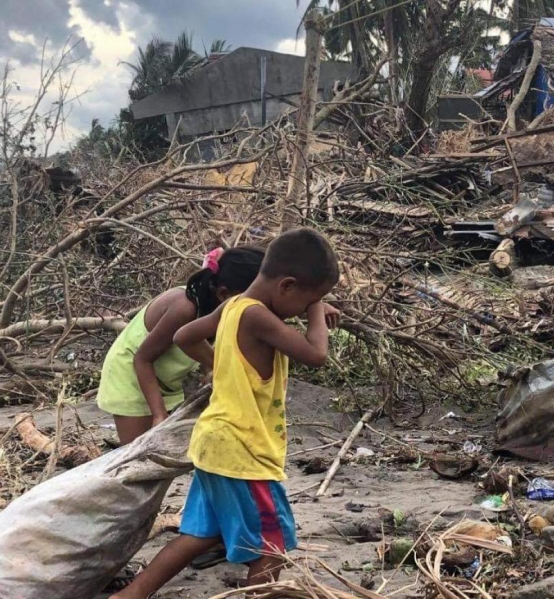 两个孩子手里拿着一个袋子，在一栋房屋的废墟附近行走。