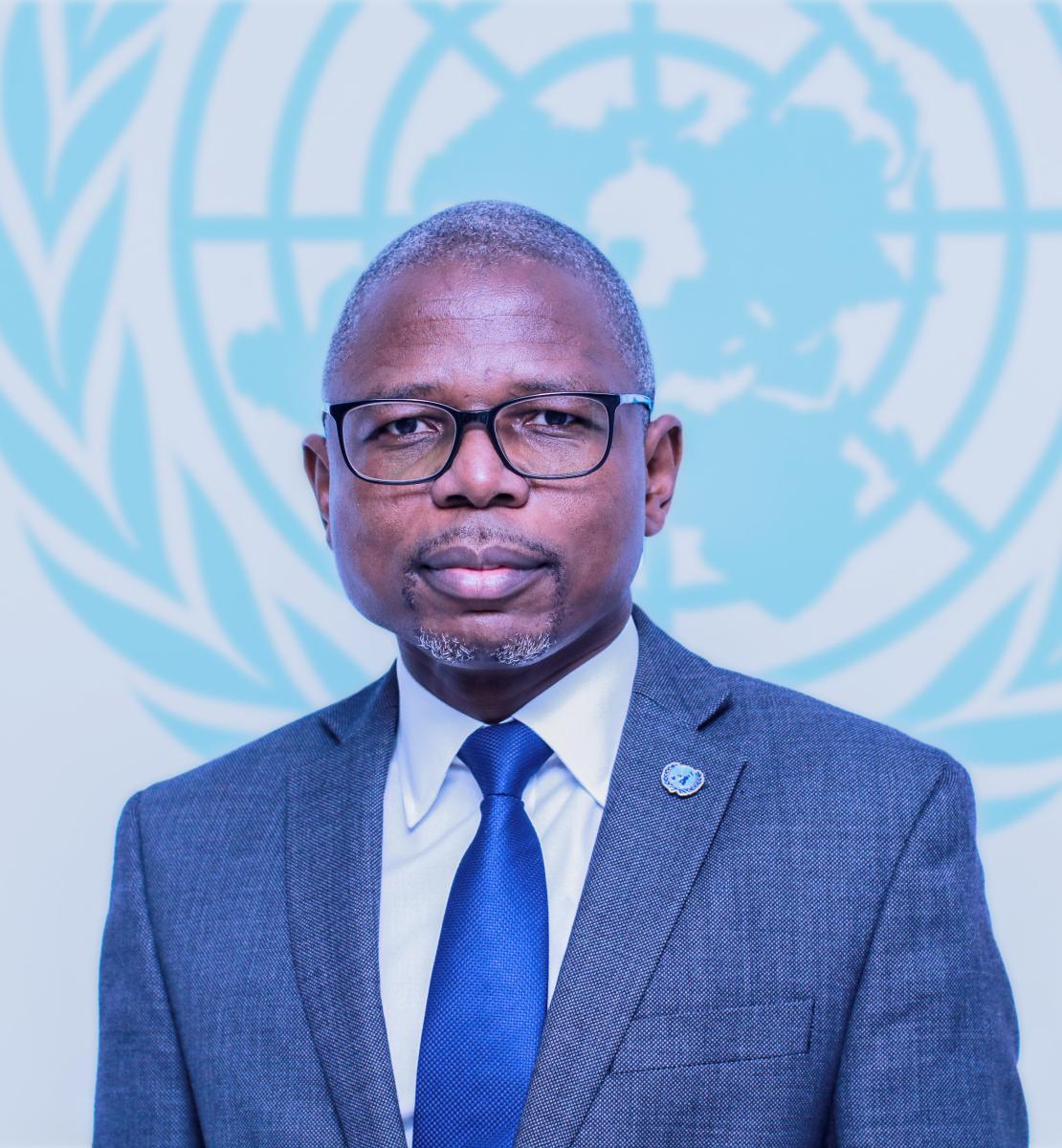 Фото мужчины в костюме и синем галстуке перед логотипом Организации Объединенных Наций.