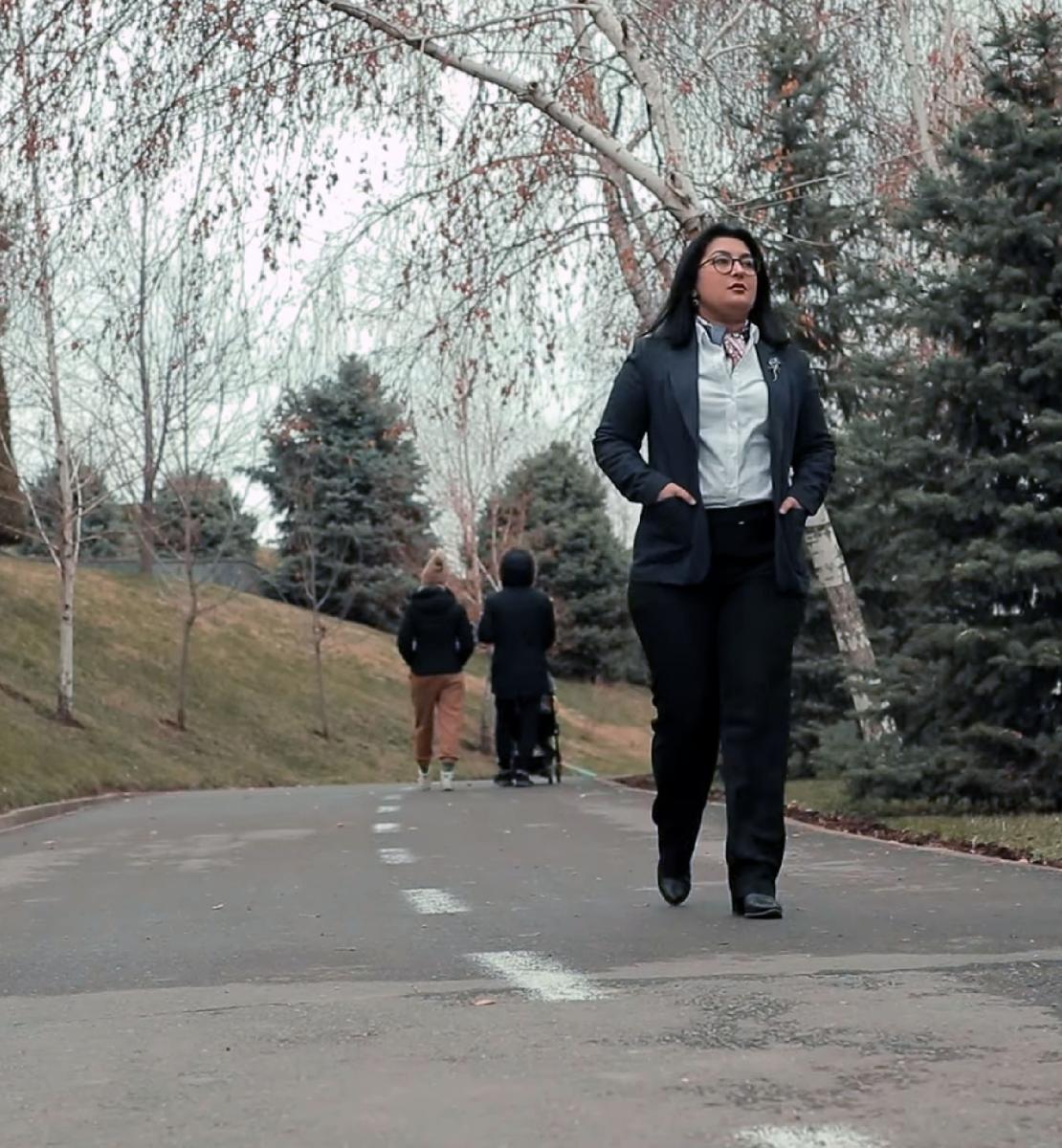 阿基达-莫基罗娃笔直地走在公园的路上，而两个人的背影，其中一个推着婴儿车从她身边走过。