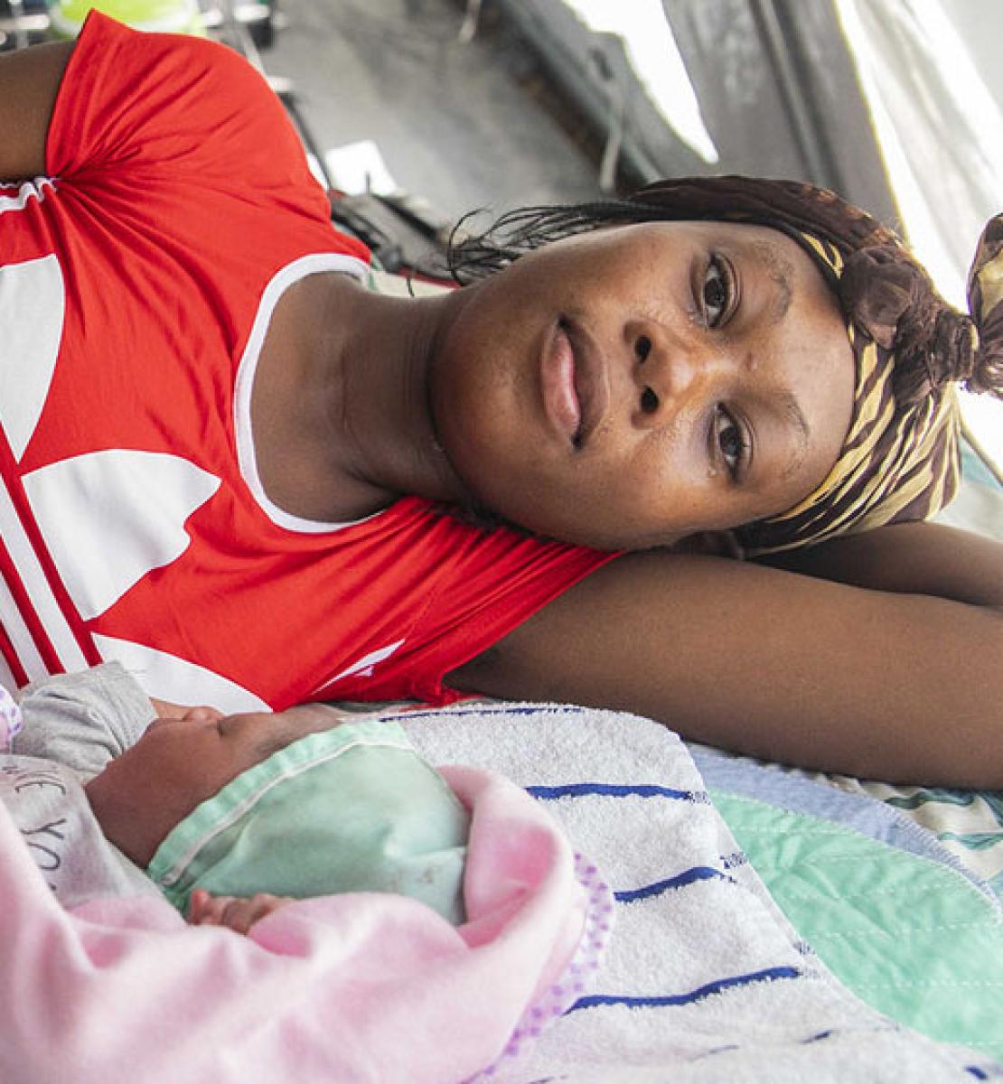 Una madre se tumba en una cama junto a su bebé recién nacido, que está envuelto en una manta rosa.