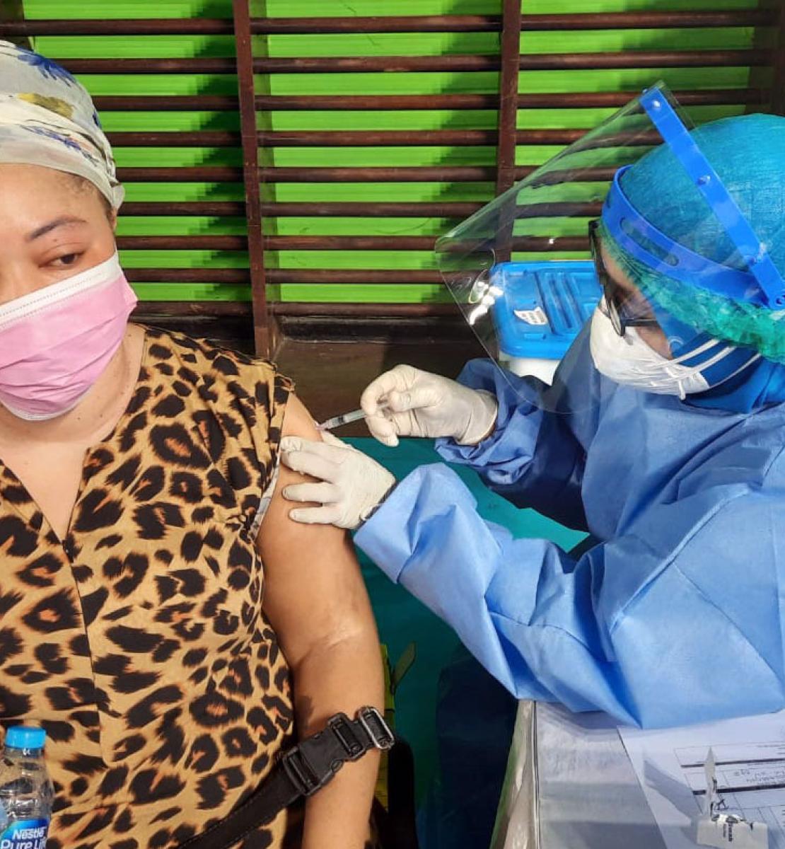 A healthcare professional gives a refugee woman, wearing a mask, her first jab of the COVID-19 vaccine.