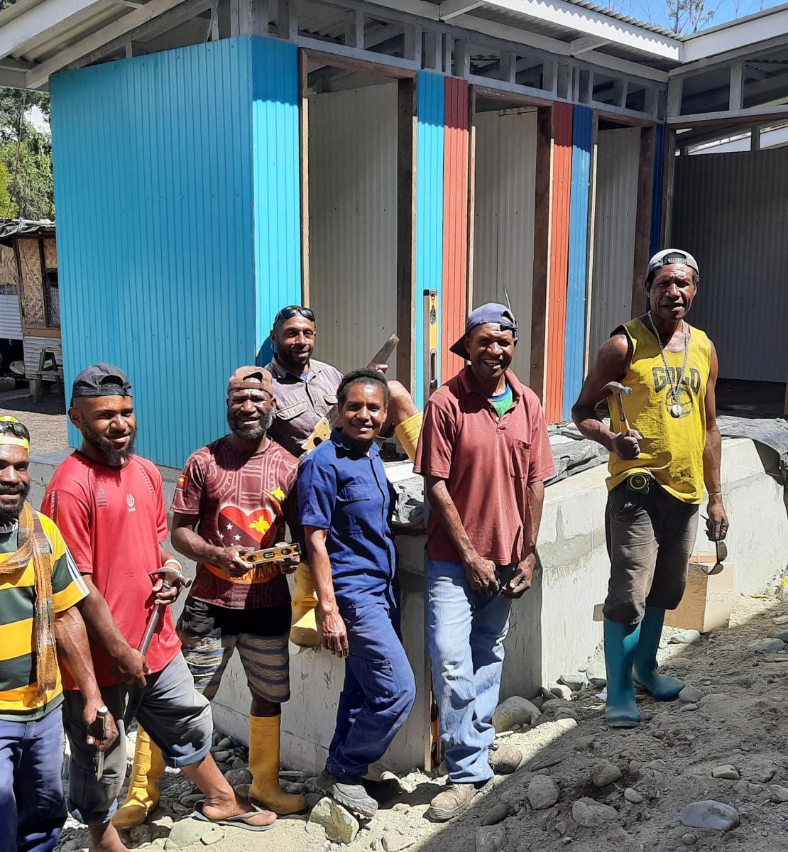 A group of men stand in front of multi-color latrines that they built. 
