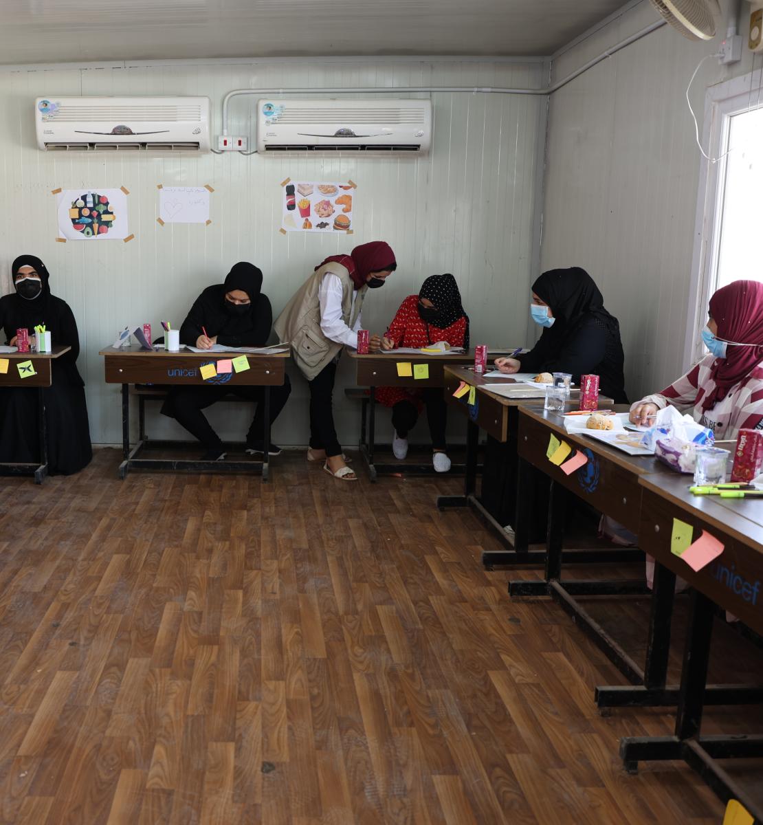 一群妇女在办公桌前工作，一名教员在帮助一名学生。
