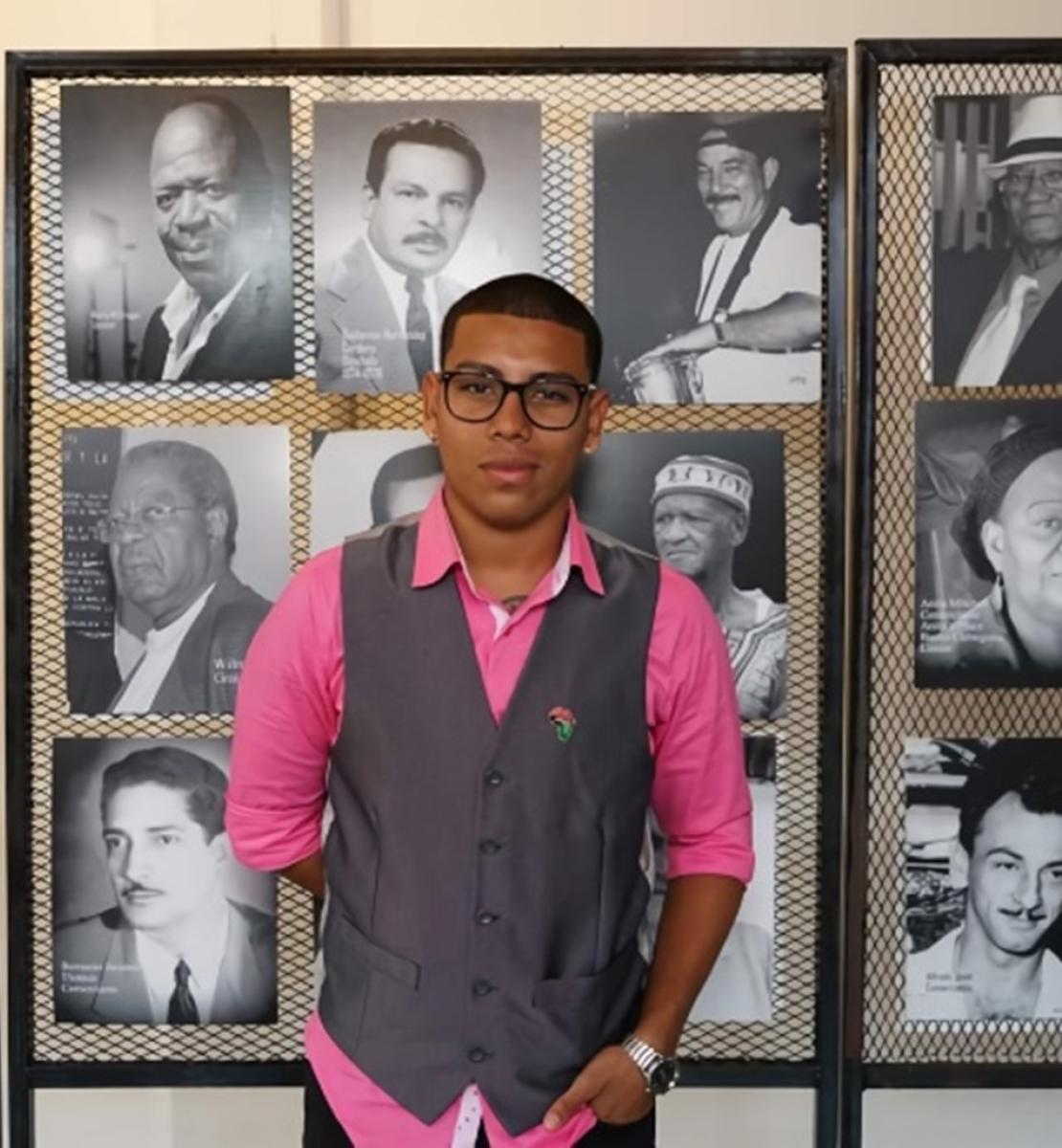 A young man stands in front of black and white portraits. 