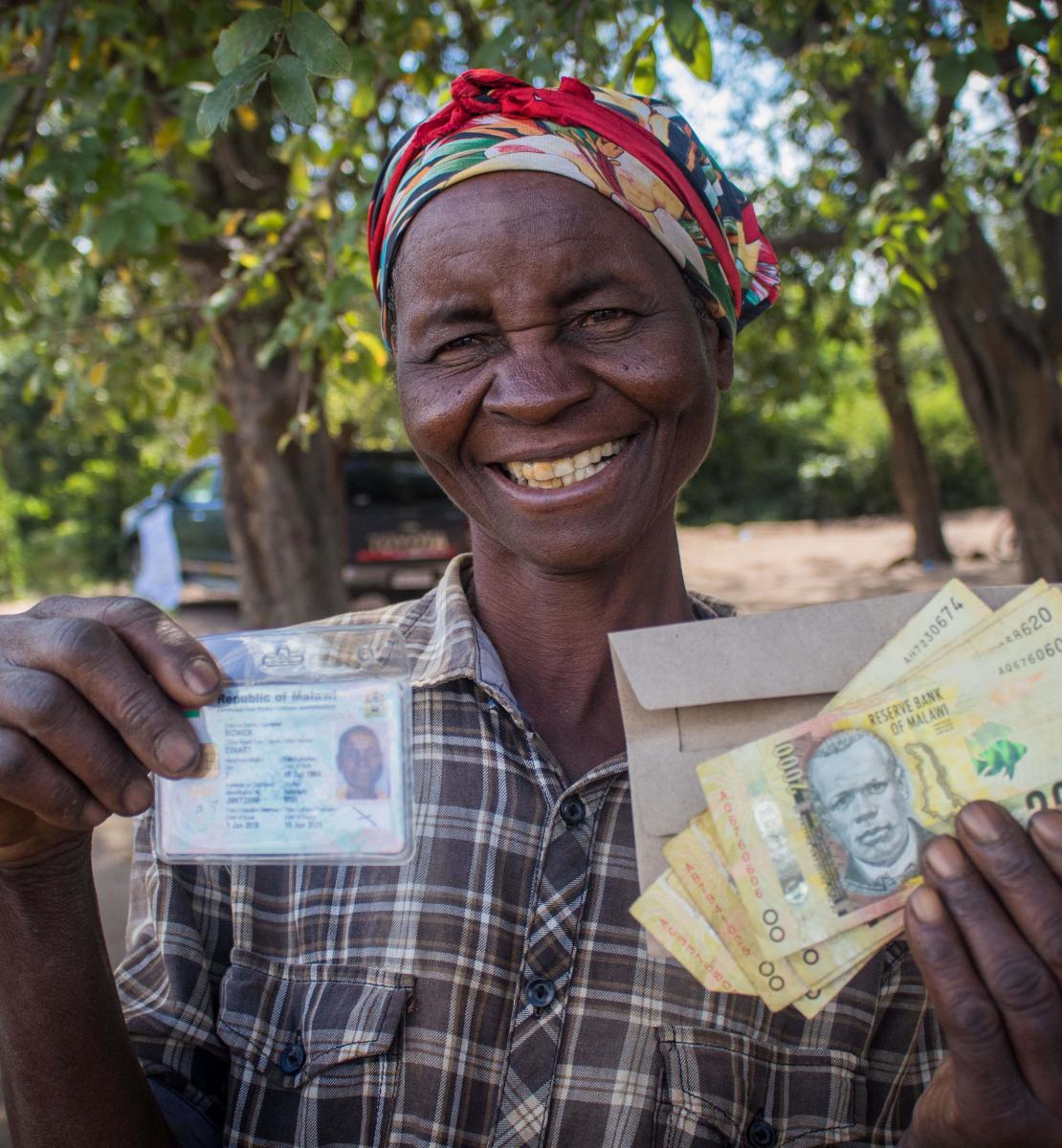 A smiling woman holds up cash assistance and her identification card. 