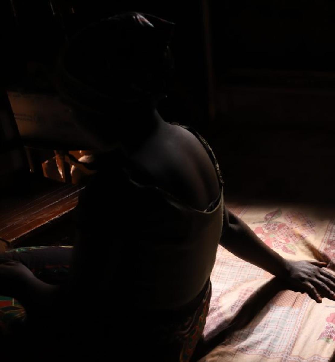 A silhouette of a girl sitting on a bed with one arm extended. 