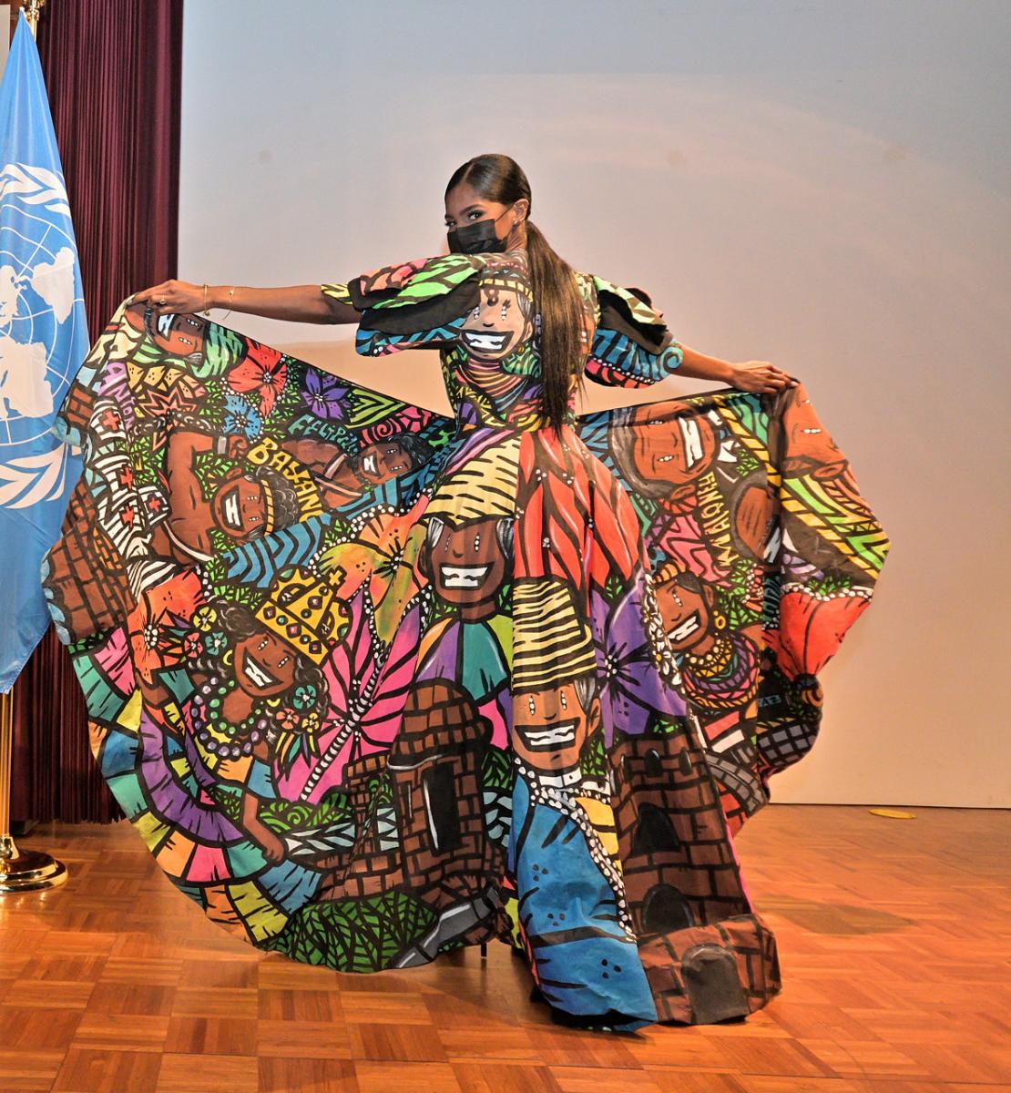 A woman stands on a stage showing a unique pattern on her colorful dress. 